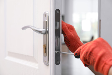 Handyman with screwdriver repairing door lock indoors, closeup