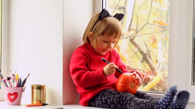 Cute Little Girl painting pumpkin for halloween at home. Autumn activity for children concept