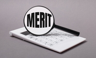 On gray background black calculator and magnifier with text MERIT. Business concept