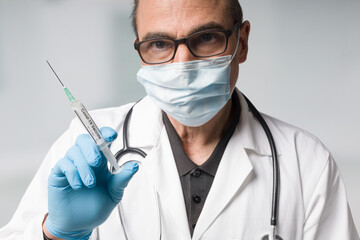 doctor with medical face mask and medical gloves presenting a syringe pulled up with a coronavirus vaccine