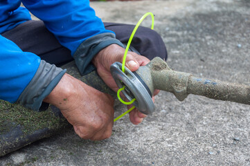 Trimmer line close-up. Gardener's hand holding a trimmer head with nylon cord cutting grass and...