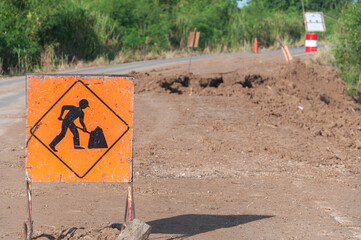 A road ahead warning sign has workers working on the road surface. The road along the canal collapsed when the water level was low. and received the vibration from the car thus causing the collapse
