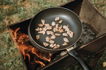 Frying pan of fried bacon, green grass on the background, cooked on the grill on a summer sunny day, summer breakfast, eating in nature.