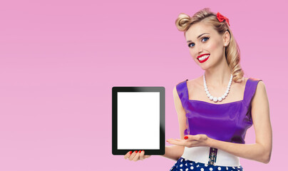 Woman showing blank tablet pc monitor, with copy space, dressed in pin up style dress in polka dot,...