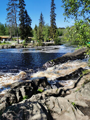 The picturesque Ahvenkoski waterfall on the Tokhmayoki River in Karelia with a suspension bridge over it on a clear summer morning..