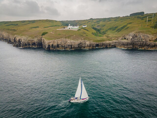 Sail boat sailing past Anvil Point lighthouse along the Jurassic Coast in Devon, South West England 