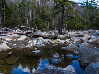 Reflection of the sky and trees in the slower flowing crystal clear Pemigewasset River in spring on the Lincoln Forest trail in the White Mountains, Lincoln, NH