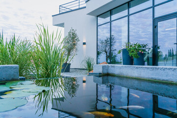 The water in the fish pond reflects the view of the glass wall of the modern home and creates a...