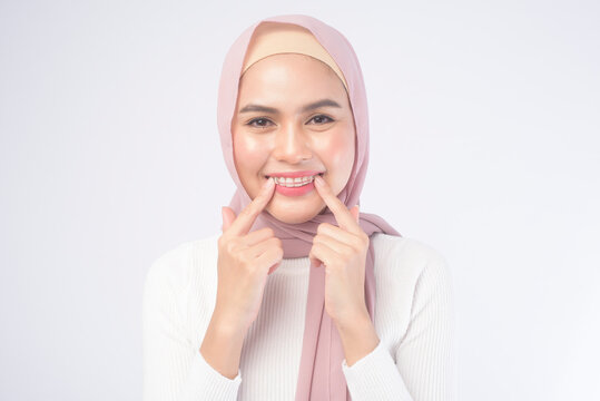 Young muslim woman holding colorful retainer for teeth over white background studio, dental healthcare and Orthodontic concept.