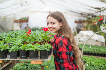 happy teen girl florist planting pot plants in greenhouse, gardening