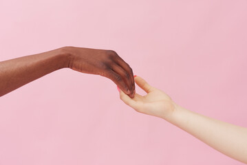 Hands of a Caucasian woman and an African American man touching each other lightly against a pink...