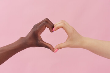 Caucasian woman and African American man show heart with their hands on pink background. The...