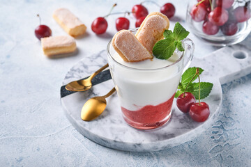 Summer cherry puff pastry with savoiardi cookies and cream cheese in glass on light grey background. Traditional tiramisu cake with fresh berries. Selective focus.