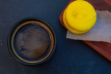 Black coffee cup with dessert on wooden pad top view. Mug of Americano, Espresso glass, sweet yellow lemon macaroon on concrete table. For coffee shop templates, cafe, confectionery concept