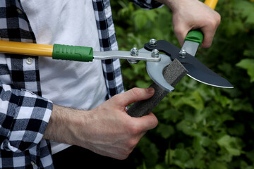 Man sharpening pruner outdoors, closeup. Gardening tools - obrazy, fototapety, plakaty