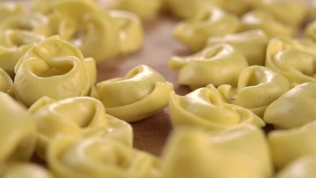 Uncooked dry stuffed tortellini shaped pasta falling on a cutting wooden board in slow motion. Macro shot