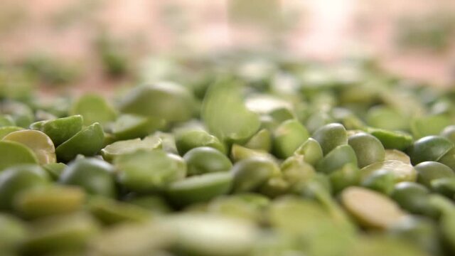 Dry green split pea falling in a heap on a wooden surface in slow motion. Macro shot. Raw uncooked legumes beans