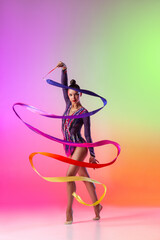 Beautiful young female rhythmic gymnast posing with bright ribbon in her hand isolated on multicolored neon background.
