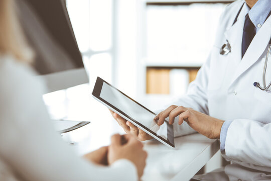 Unknown male doctor and patient woman discussing current health examination while sitting in clinic and using tablet computer. Perfect medical service in hospital. Medicine and healthcare concept