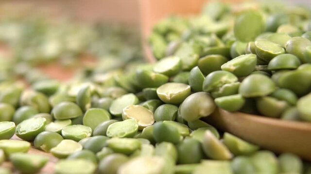 Dried split green peas fall on a pile in a wooden spoon on a wood surface. Rustic agriculture view. Macro shot. Slow motion. Vegan healthy food concept