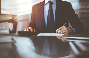 Unknown man accountant in blue blazer use calculator and computer while staying at home during...