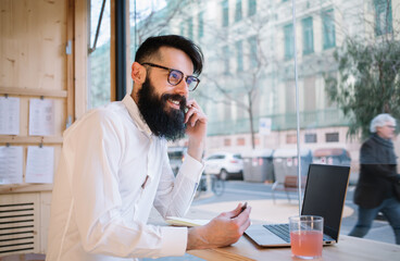 Optimistic bearded man talking on smartphone in cafe