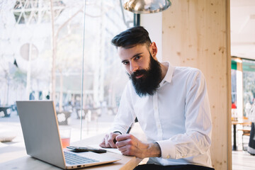 Thoughtful male writer doing remote work in cafe with devices