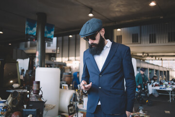 Serious stylish bearded man choosing retro objects on flea market