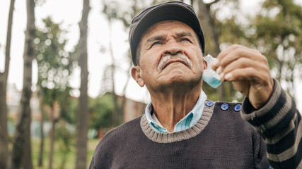 elderly man taking off his mask enjoying the outdoors in the park taking a walk