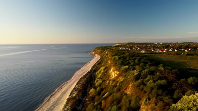 Top view of the Curonian spit and Baltic sea in Kaliningrad filmed by the drone at warm summer day. Aerial footage of the ridge with little town on it and blue ocean. Living on cliff next to coastline