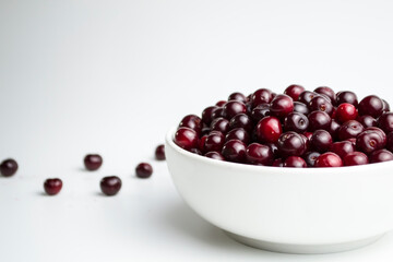 Dark red cherry in a white cup on a white background. And scattered cherries nearby.