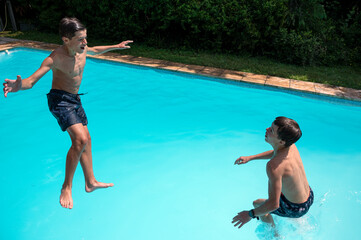 Naklejka premium Deux garçons adolescents qui jouent à sauter dans l'eau d'une piscine en extérieur en été