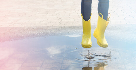 Happy child in yellow wellington boot jumps in a puddle of water after rain. Cheerful baby on a...