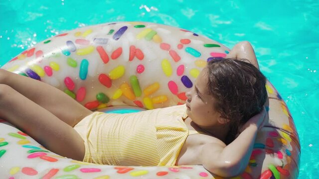 Kid lies on an inflatable ring in the pool. Little girl Swimming In Pool on orange inflatable rubber ring. Holidays, Vacations, Recreations, Sport, Children, Water, Hotel, Summer