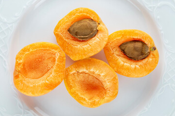 Four half ripe apricot on a white earthenware dish, close-up, top view.