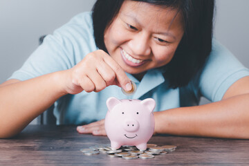 Woman happy smiling hand putting coin into piggy bank on wooden table with save money concept, Finance or investment saving money for future conceptual