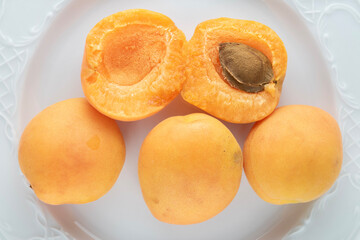 Three whole and two half ripe apricots on a white earthenware dish, close-up, top view.