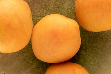Several organic ripe apricots on a ceramic plate, close-up, top view.