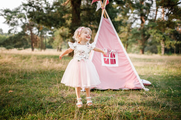 cute little girl is having fun near wigwam in a summer field on sunny day. Young family spending time together on vacation, outdoors. The concept of summer holiday © Andriy Medvediuk