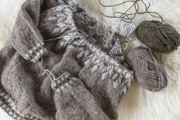 Fototapeta na wymiar Beige Icelandic wool knitted lopapeysa sweater in progress with yarn balls and needles