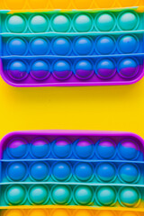 Two parts of colorful rainbow anti stress pop it toys on yellow background. Creative concept. Flat lay, top view.
