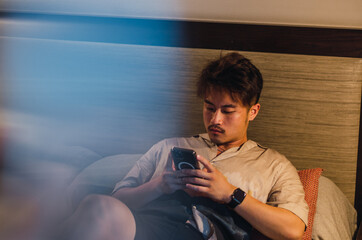 Young relaxed asian man traveller using smartphone, computer and taking notes in hotel room while on vacation