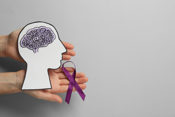 Top view of woman holding human head cutout with brain and purple ribbon on light grey background,...