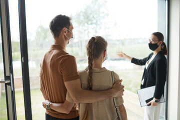 Back view portrait of young couple listening to real estate agent during apartment tour, copy space