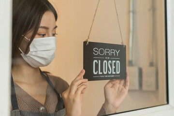 Asian young owner retail,coffee shop woman turning sign board to closed with wearing face...