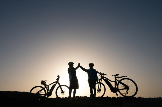 Silhouette of a couple of sporty people near their bicycles on the cliff rocks enjoying freedom and healthy lifestyle - Powered by Adobe