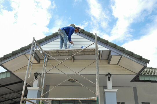 a worker standing on a scaffolding while painting house gable (selective focus), concept risk management, safety working at height