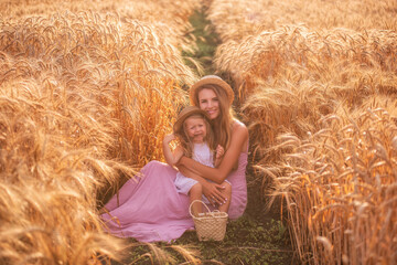 Close-up portrait of mother with daughter in straw hats in wheat field with dew drops. Young woman...
