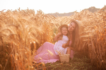 Close-up portrait of mother with daughter in straw hats in wheat field with dew drops. Young woman...