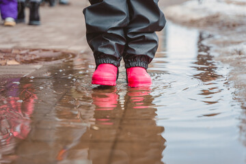 The feet of a child in pink rubber boots stomp through puddles